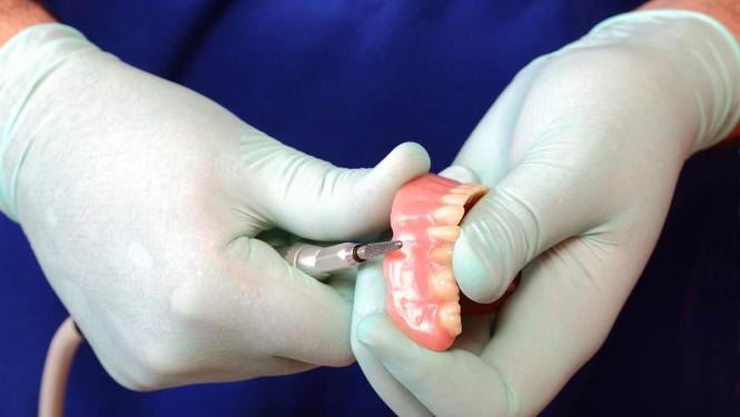 Zobu tehniķa rokas ar gumijas cimdiem. Rokās zobu protēze