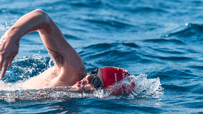 Ūdens tilpnē peldošs cilvēks ar sarkanu peldcepuri