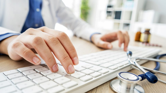 Vīrieša plaukstas uz datora klaviatūras, uz galda fonendoskops