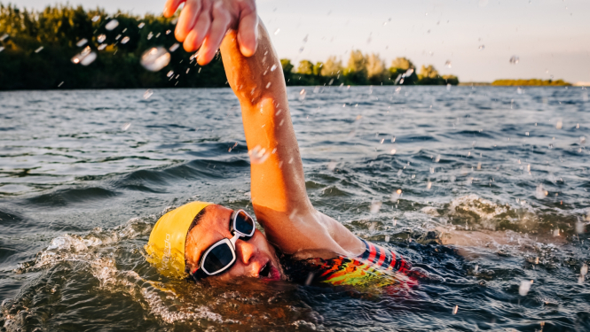 Ūdens tilpņē peldošs cilvēks dzeltenā peldcepurē