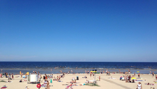 Pludmale, jūra, jūras smiltis un fonā sauļojas cilvēki