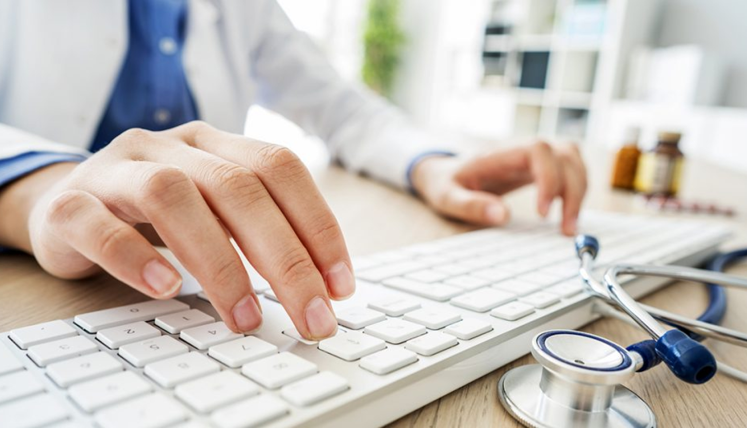 Vīrieša plaukstas uz datora klaviatūras, uz galda fonendoskops