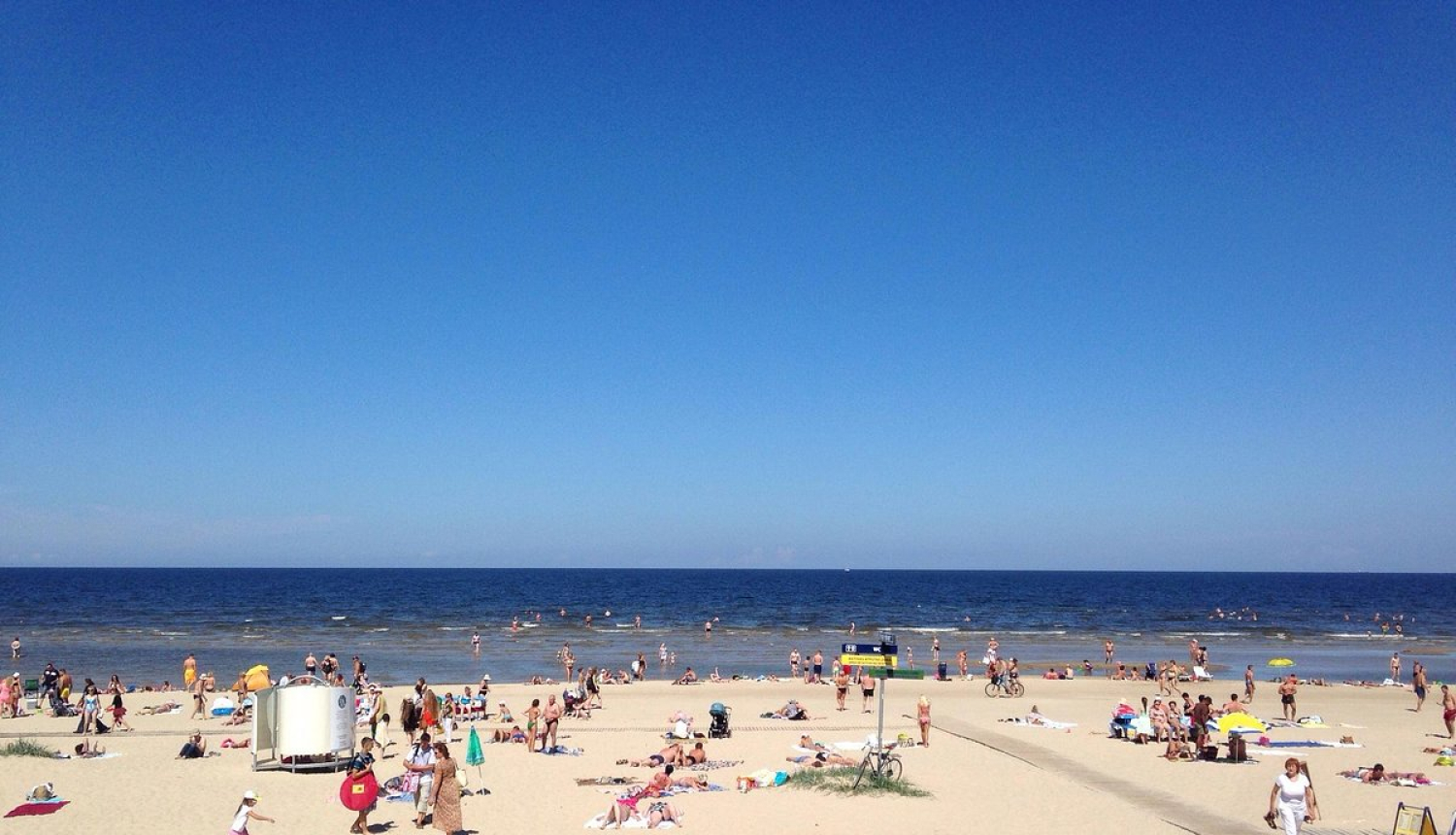 Zilas debesis, pludmales smiltis, jūra un cilvēki