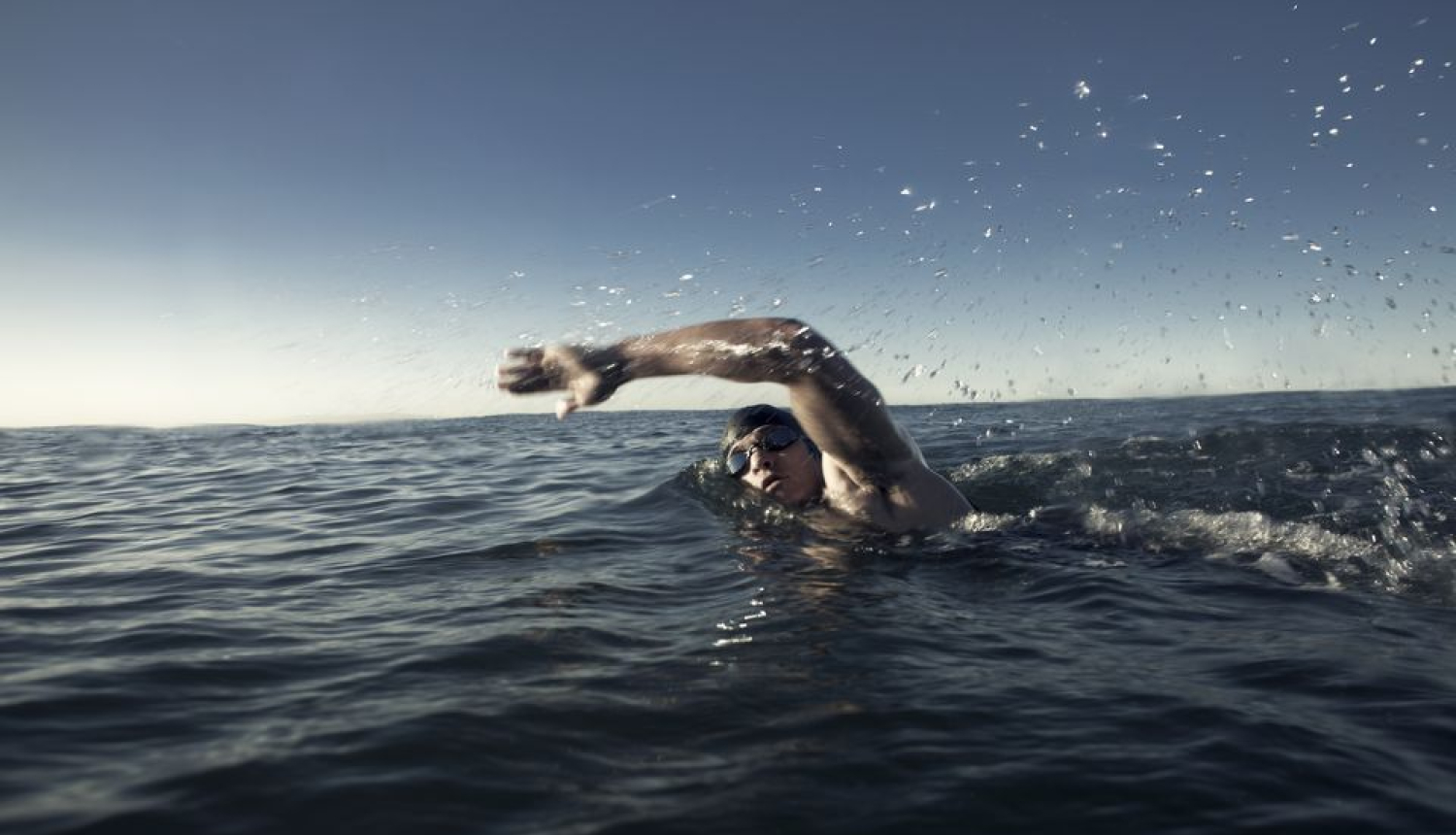 Peldošs cilvēks jūrā ar peldbrillēm un peldcepuri